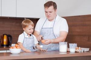 papà e figlio nel cucina, padre insegna bambino per rompere uova in un' ciotola. cucinando foto