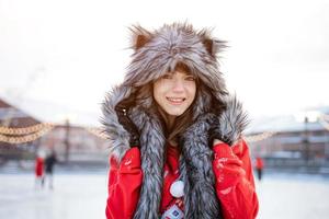 felice giovane donna in cappello lupo in inverno sulla pista di pattinaggio in posa in un maglione rosso foto