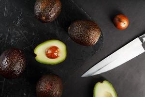 maturo avocado nel un' cestino su un' nero tavolo, con un' tagliare frutta e un' pietra. foto