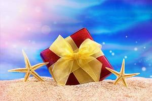 festivo rosso scatola con arco e stella marina su spiaggia. concetto di vacanza nel tropicale Paesi. Natale, nuovo anno, compleanno. copia spazio foto