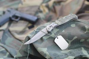 esercito cane etichetta gettone con coltello e pistola menzogna su piegato camuffare verde tessuto foto