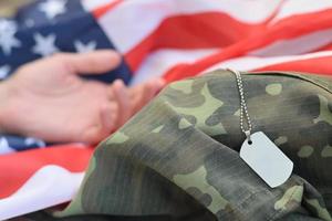 argenteo militare perline con cane etichetta e mano di morto soldato su unito stati tessuto bandiera e camuffare uniforme foto