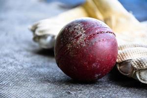 formazione cricket sport attrezzature su pavimento, pelle sfera, guanti e pipistrello, morbido e selettivo messa a fuoco su sfera. foto