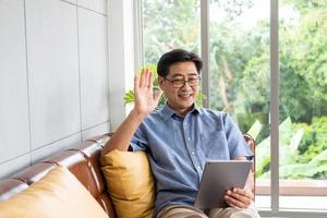 anziano asiatico uomini Sorridi e sensazione contento mentre utilizzando smartphone tavoletta per video chiamata con il suo famiglia. Internet senza fili tecnologia con la pensione persona a casa. foto