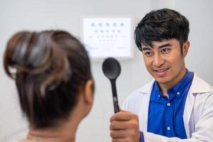 selettivo messa a fuoco a optometrista viso. mentre medico utilizzando torcia e soggettivo rifrazione per esaminare occhio visivo sistema di Sambuco paziente donne con professionale macchina prima fatto occhiali. foto