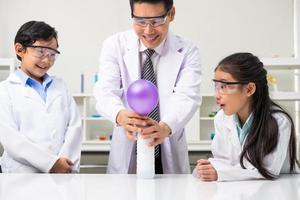 giovane asiatico bambini indossare bianca scienziato toga e fare chimico test tubo mentre studia, apprendimento nel scienza aula con insegnante. giovane bambini formazione scolastica concetto di sperimentare, divertimento e godere aula foto