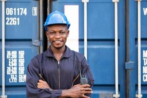 selettivo messa a fuoco a viso di nero africano logistica lavoratore indossare sicurezza attrezzatura, dai un'occhiata e ispezione il condizione di contenitore mentre parlando e comunicare con il suo squadra di Radio dispositivo. foto