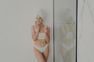 bella donna in piedi in bagno dopo la doccia mattutina e applicare una crema idratante sul viso foto