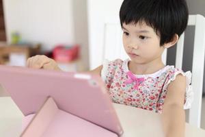 poco asiatico ragazza giocando digitale tavoletta a casa foto