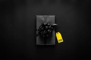 un' nero regalo scatola con nastro e giallo prezzo etichetta mette su nero sfondo. nero Venerdì concetto. foto