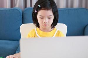 poco asiatico ragazza alunno studia in linea utilizzando il computer portatile computer a casa foto