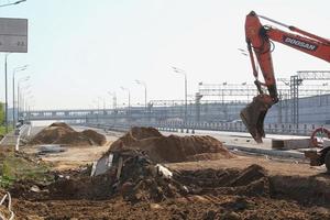 scavatrice macchinari Lavorando su costruzione luogo di nuovo strada per il città. arancia terna scava sabbia e ghiaia. concetto di rinnovamento edifici, ponti e strade foto