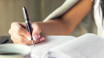 giovane donna giusto mano scrittura piani su piccolo diario nel bar vicino su foto