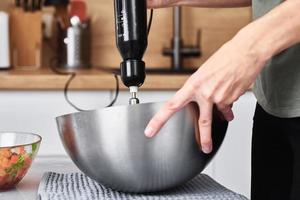 donna nel cucina cucinando un' torta. mani battere il Impasto con un elettrico miscelatore foto