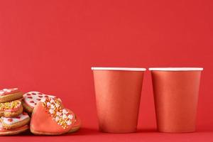 decorato cuore forma biscotti e Due carta caffè tazze su il rosso sfondo. san valentino giorno cibo concetto foto