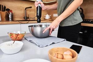 donna nel cucina cucinando un' torta. mani battere il Impasto con un elettrico miscelatore foto