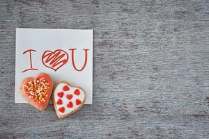 Due cuore forma biscotti e carta foglio con iscrizione io amore voi su il grigio sfondo. san valentino giorno concetto foto