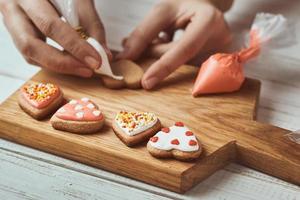 decorazione Pan di zenzero biscotti con glassatura. donna mano decorare biscotti nel forma di cuore, avvicinamento foto