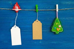 Marrone e bianca vuoto carta prezzo tag o etichette impostato e Natale decorazioni sospeso su un' corda su il blu di legno sfondo. foto