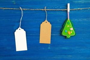 Marrone e bianca vuoto carta prezzo tag o etichette impostato e Natale provato decorazioni sospeso su un' corda su il blu di legno sfondo. foto