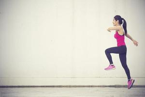 lato Visualizza tiro di in forma giovane donna fare cardio intervallo formazione contro grigio sfondo. fitness femmina esercizio all'aperto nel mattina.annata colore foto