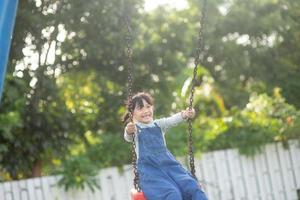 contento poco asiatico ragazza giocando swing all'aperto nel il parco foto