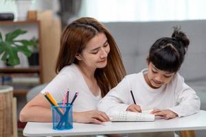 bellissimo asiatico donna porzione sua figlia con compiti a casa a casa. foto