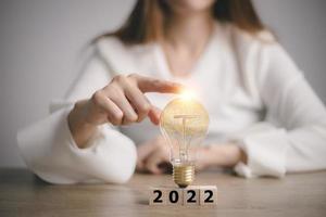 mano toccante su leggero lampadina su legna bloccare con parola 2022, nuovo idea concetto con innovazione e ispirazione, foto