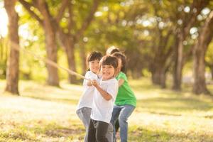 bambini giocando tirare di guerra a il parco su tramonto foto