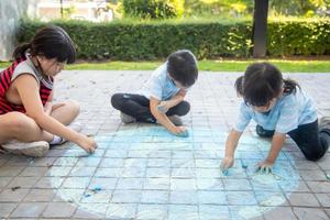 asiatico bambini giocare all'aperto. bambino ragazza disegna un' pianeta globo con un' carta geografica di il mondo colorato gesso su il marciapiede, asfalto. terra, pace giorno concerto. foto