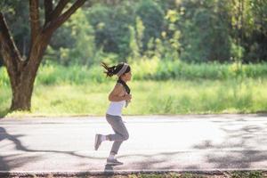 contento bambino ragazza in esecuzione nel il parco nel estate nel natura. caldo luce del sole bagliore. asiatico poco è in esecuzione nel un' parco. all'aperto gli sport e fitness, esercizio e concorrenza apprendimento per ragazzo sviluppo. foto