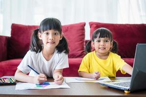 Due asiatico bambino ragazza studenti studia in linea con insegnante di video chiamata insieme. fratelli siamo homeschooling con computer il computer portatile durante quarantena dovuto per covid 19 pandemia. foto