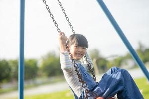 contento poco asiatico ragazza giocando swing all'aperto nel il parco foto