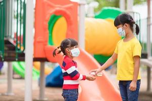 nuovo normale stile di vita, sociale distanziamento concetto. contento bambini indossare viso maschera avendo divertimento su a terreno di gioco proteggere coronavirus covid19, foto