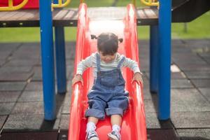 asiatico bambino ragazza giocando su il all'aperto terreno di gioco. bambini giocare nel scuola o scuola materna cortile. salutare estate attività per bambini. foto