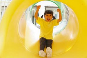 bambino giocando su all'aperto terreno di gioco. bambini giocare su scuola o scuola materna cortile. attivo ragazzo su colorato diapositiva e oscillazione. salutare estate attività per bambini. foto