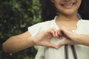 poco ragazza mani fabbricazione un' cuore forma su bianca sfondo foto