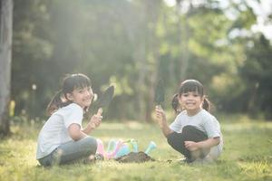 asiatico fratello piantare giovane albero su nero suolo insieme come Salva mondo nel giardino su estate giorno. piantare albero. infanzia e all'aperto tempo libero concetto. foto