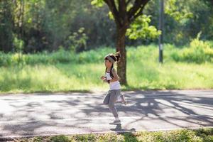 contento bambino ragazza in esecuzione nel il parco nel estate nel natura. caldo luce del sole bagliore. asiatico poco è in esecuzione nel un' parco. all'aperto gli sport e fitness, esercizio e concorrenza apprendimento per ragazzo sviluppo. foto