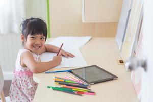 poco asiatico bambino utilizzando un' matita per Scrivi su taccuino a il scrivania foto