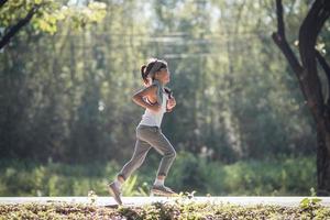 contento bambino ragazza in esecuzione nel il parco nel estate nel natura. caldo luce del sole bagliore. asiatico poco è in esecuzione nel un' parco. all'aperto gli sport e fitness, esercizio e concorrenza apprendimento per ragazzo sviluppo. foto