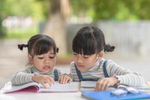 Due alunno poco asiatico ragazze lettura il libro su tavolo foto