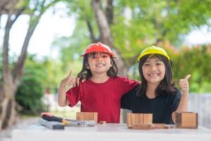 asiatico fratelli ragazze indossare ingegneria cappelli edificio Casa a partire dal il di legno giocattolo. per apprendimento e migliorare sviluppo, poco architetto. foto