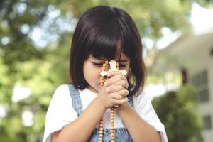 poco asiatico ragazza preghiere con Tenere il attraverso, cristiano concetto. foto