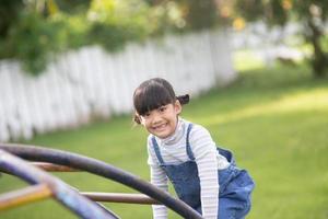 asiatico bambino ragazza giocando su il all'aperto terreno di gioco. bambini giocare nel scuola o scuola materna cortile. salutare estate attività per bambini. foto