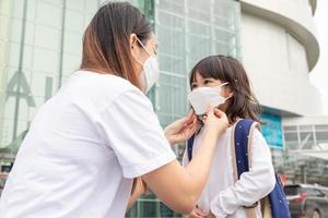 asiatico madre aiuta sua figlia indossare un' medico maschera per protezione covid-19 o coronavirus scoppio preparare per partire per scuola quando indietro per scuola ordine. foto