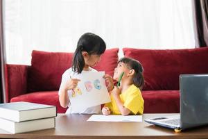 Due asiatico bambino ragazza studenti studia in linea con insegnante di video chiamata insieme. fratelli siamo homeschooling con computer il computer portatile durante quarantena dovuto per covid 19 pandemia. foto