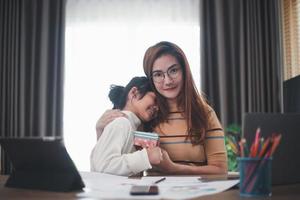 contento La madre di giorno. giovane donna mamma ottenere Congratulazioni a partire dal eccitato carino poco figlia a casa, bambino dando madre regalo scatola mentre lei Lavorando su il computer portatile. famiglia vacanze concetto foto