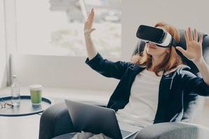 donna d'affari in occhiali per realtà virtuale che testa un metodo innovativo per il business, lavorando da remoto foto