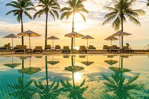 bellissimo ombrellone di lusso e sedia intorno alla piscina all'aperto in hotel e resort con palme da cocco al tramonto o all'alba sky foto